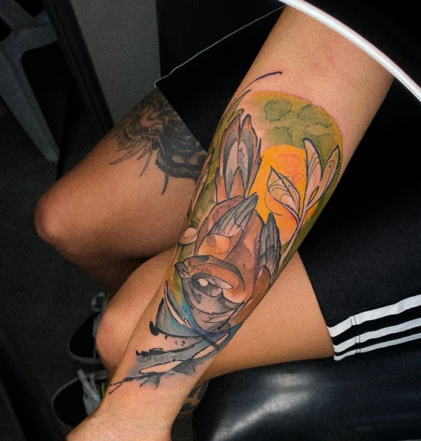 Tatuagem colorida com folhas e elementos orgânicos no braço