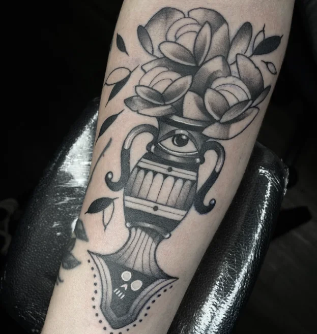 Tatuagem em preto e cinza de pincel, olho e flores no braço
